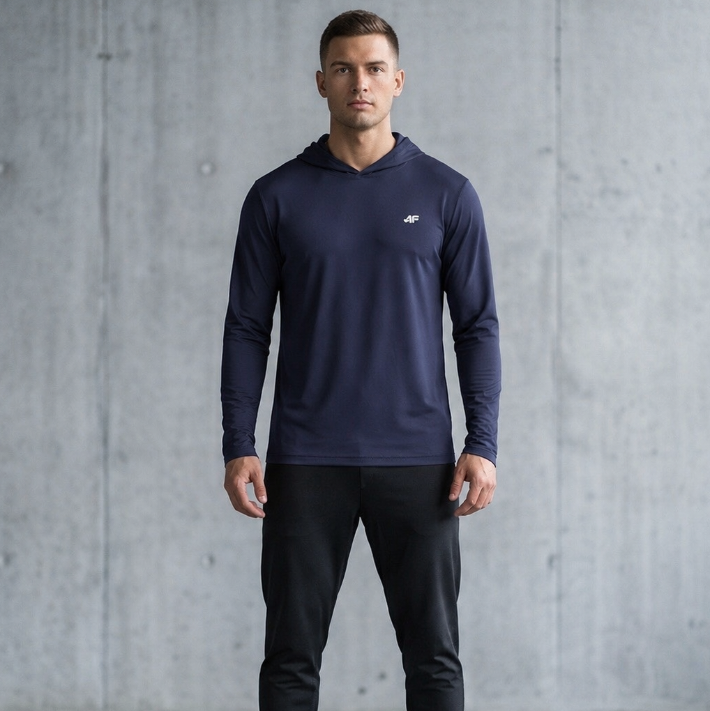 Man wearing a navy long-sleeve shirt and black pants against a gray concrete wall.