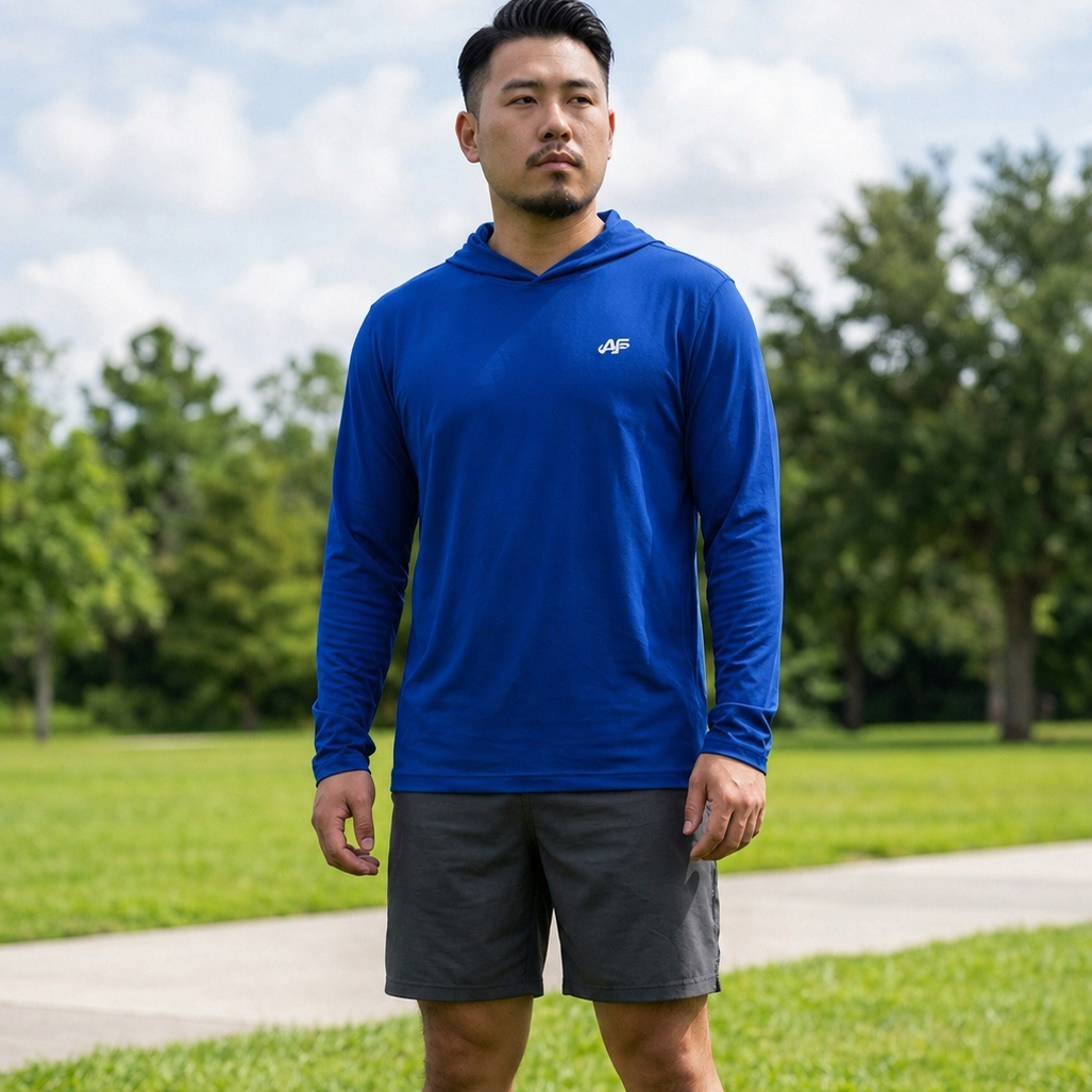 Man wearing a blue hoodie and gray shorts standing on grass with trees in the background