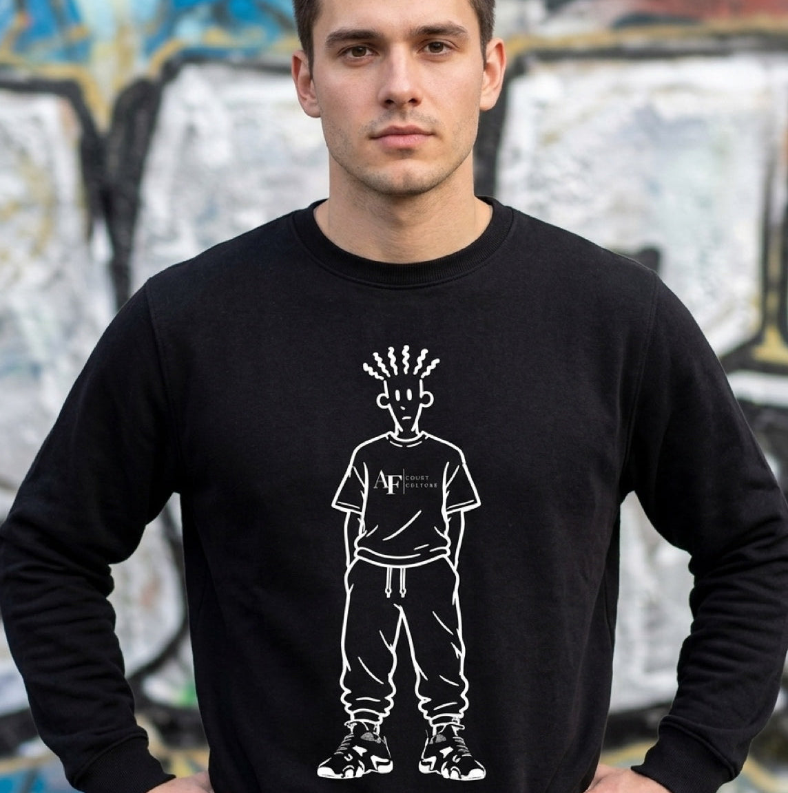Man wearing a black sweatshirt with a graphic design in front of a graffiti-covered wall.