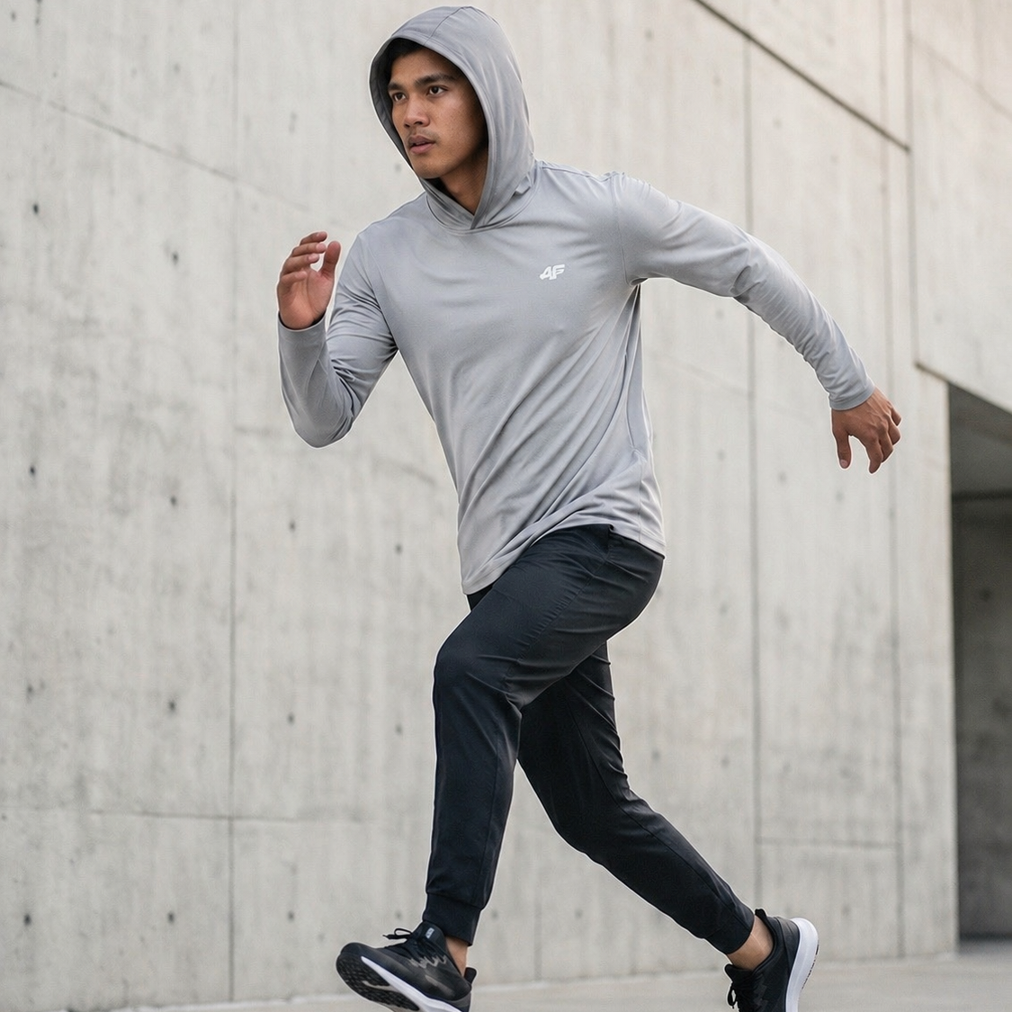Person wearing a gray hoodie and black pants running against a concrete wall.