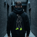 Person wearing a black hoodie with a graphic design on the back, walking down a narrow alley.