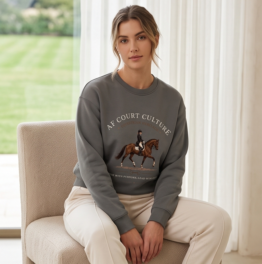 A woman sits on a beige armchair in a bright room, wearing a dark gray sweatshirt with a horse graphic and the words 'AF COURT CULTURE' on the front, paired with cream-colored pants.