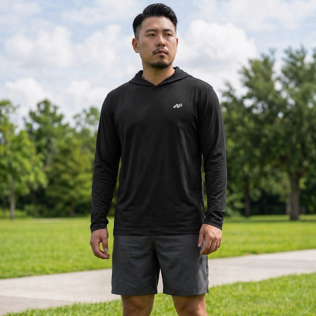 Man wearing a black hoodie and gray shorts standing on grass with trees in the background