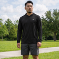 Man wearing a black hoodie and gray shorts standing on grass with trees in the background