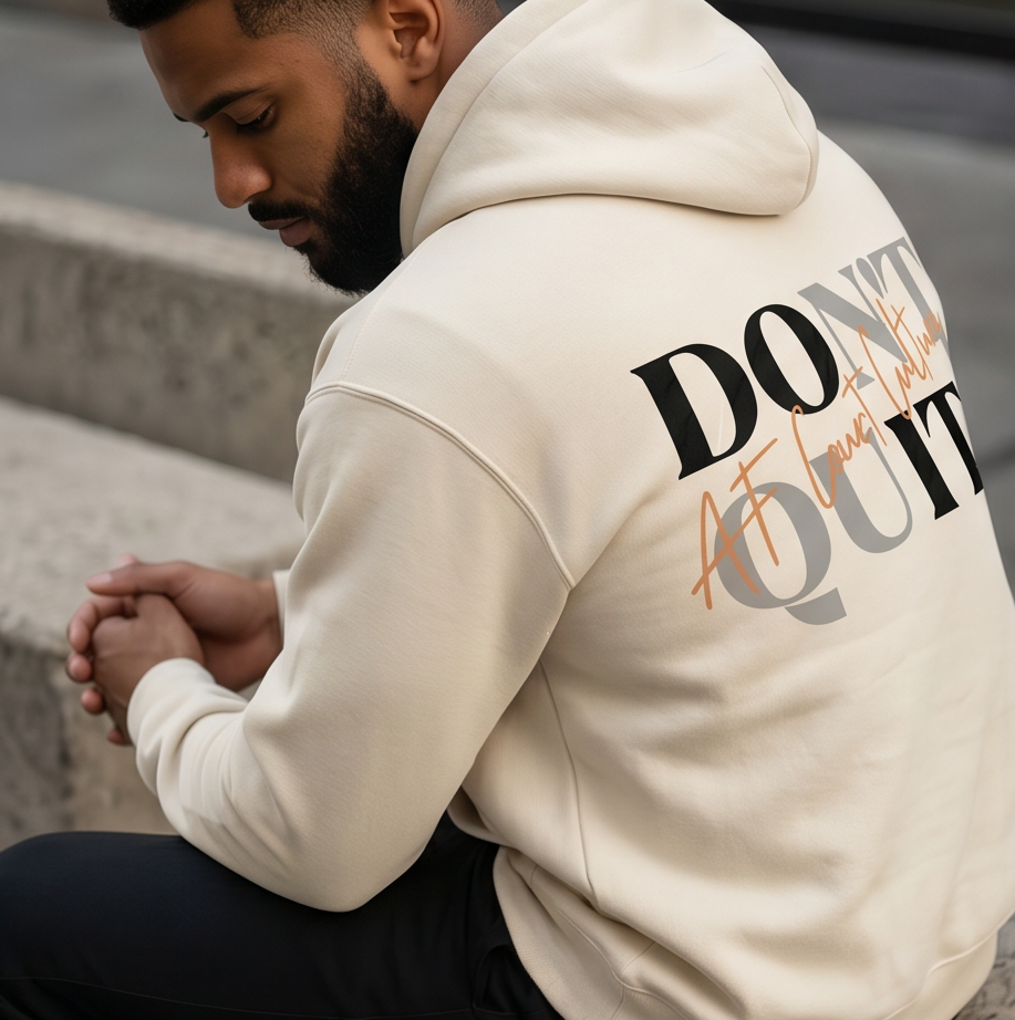 Person wearing a beige hoodie with text on the back, sitting on steps.