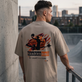 Person wearing a beige t-shirt with a basketball design, standing on a rooftop with cityscape in the background.