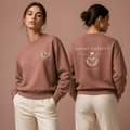 Two women modeling a dusty rose sweatshirt and cream trousers in a studio setting with a matching dusty rose background. The front view shows a small crest logo on the left chest, and the back view shows 'COURT SOCIETY EST.