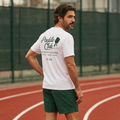 Man wearing a white t-shirt with text and green shorts on a red track.