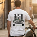Man wearing a white t-shirt with a motorcycle graphic and text, sitting on a motorcycle.