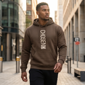 Man wearing a brown hoodie with 'CHISEN ONE' text in an urban setting