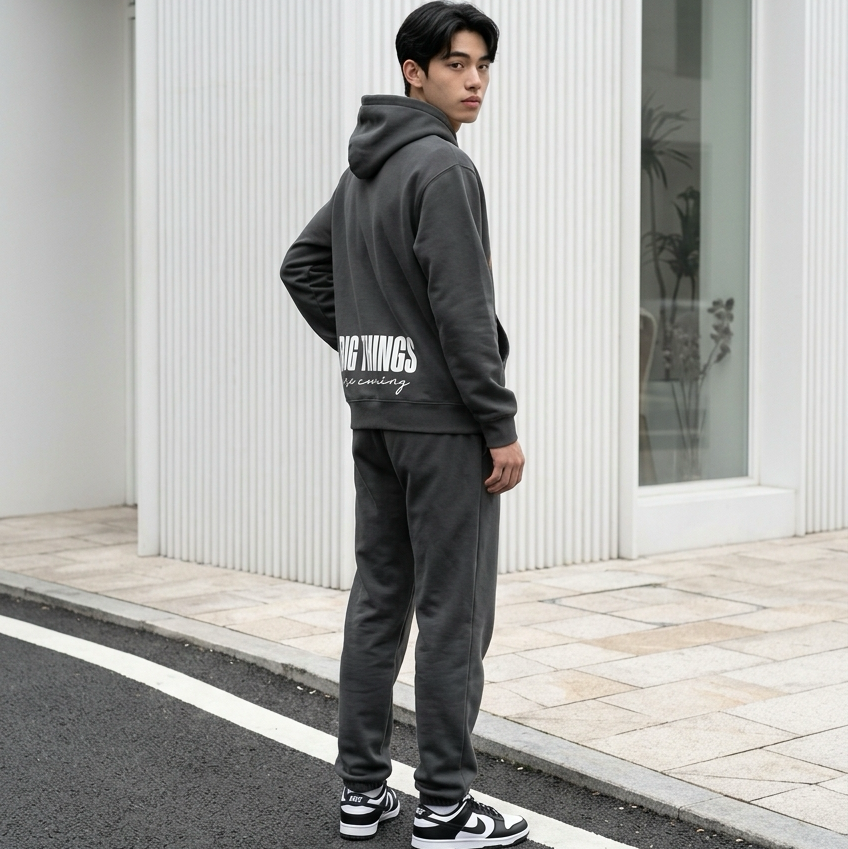 Person wearing a gray hoodie and pants with text, standing on a street.