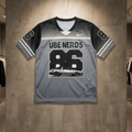 Gray sports jersey with 'UBE NERDS 86' printed on it, displayed against a concrete wall in a store.
