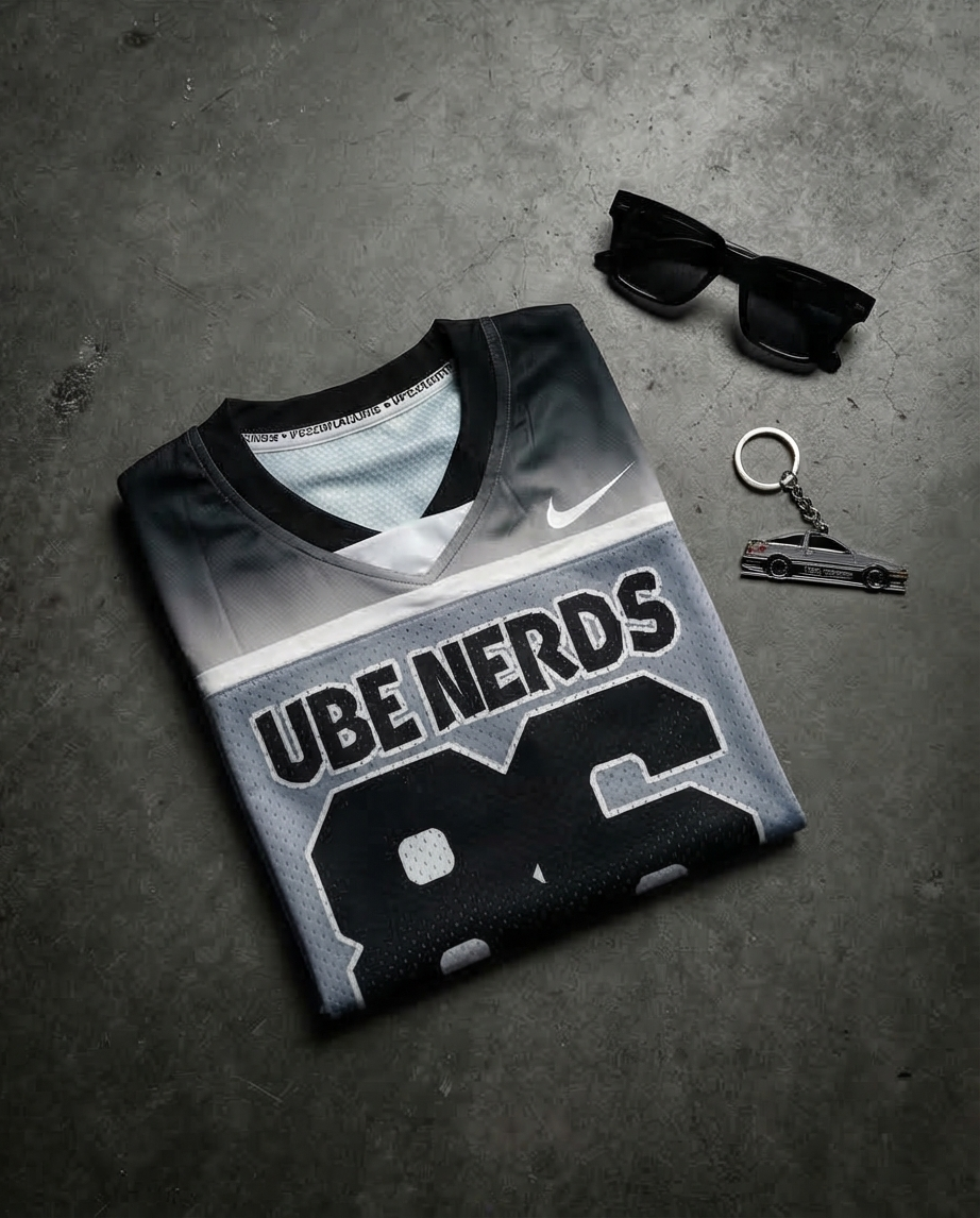 Gray sports jersey with 'UBE NERDS' text on a gray surface with sunglasses and a keychain.