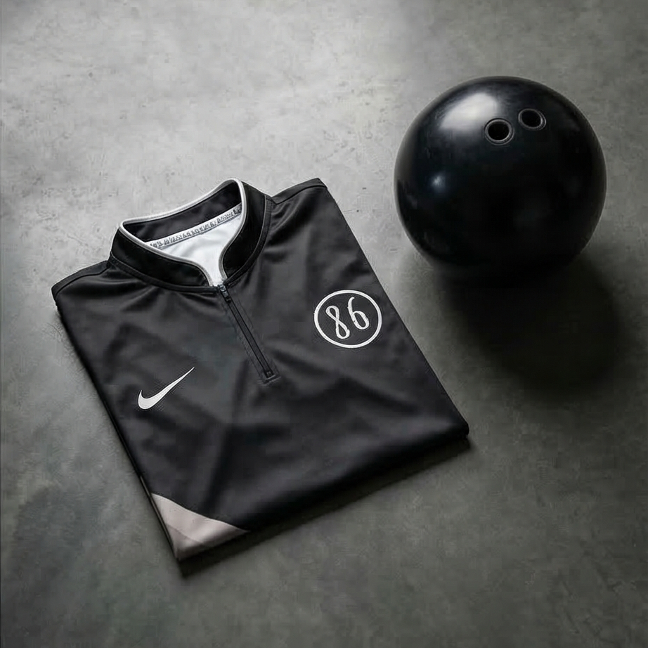 Black quarter-zip pullover with a logo and a black bowling ball on a gray surface